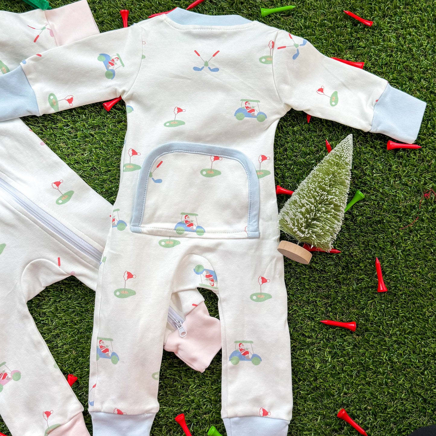 Back view of holiday golf baby onesie with blue trim, two-way zipper, and decorative back panel, displayed on turf with Christmas props.