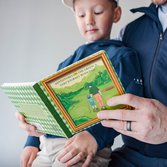 Dad reading to son kids golf book. Front cover shown with title Adventures on the Green: A Golf Journey with Dad. Illustrated picture of Dad and child walking on a fairway.
