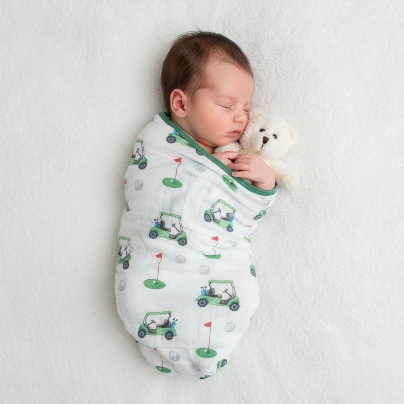 Newborn baby sleeping while swaddled in a golf-themed muslin blanket with green trim and playful golf cart print