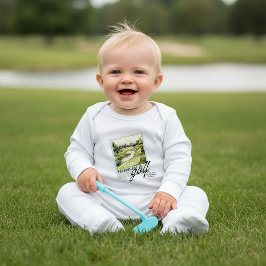 Smiling baby sitting on a golf course wearing white Aster and Ace “Happiness Is Golf” coverall and holding a toy golf club.