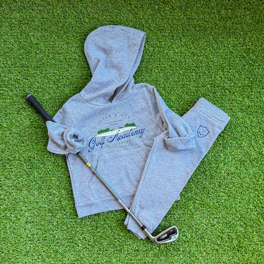 Heather grey Aster and Ace Golf Academy kids hoodie and matching crest sweatpants set styled on turf beside a junior golf club