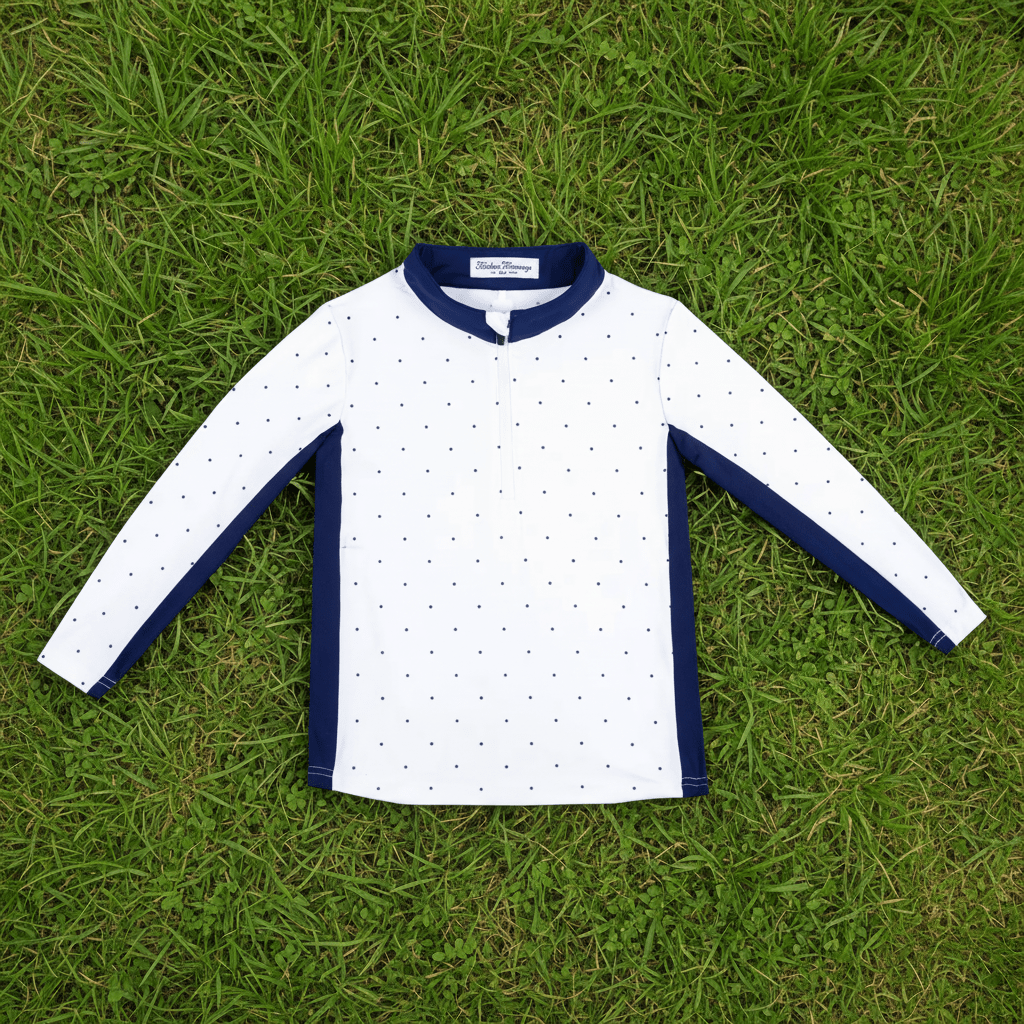A children's long-sleeve performance quarter zip laid flat on green grass. The pullover is white with small navy stars pattern, featuring solid navy blue trim at the collar, sleeve cuffs, and side panels.