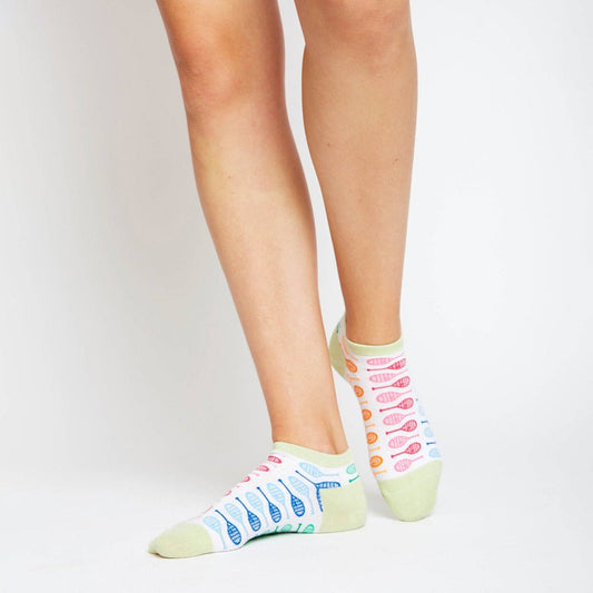 Child standing in white ankle socks with pastel green trim and bright tennis racket pattern, shown from mid-calf down.