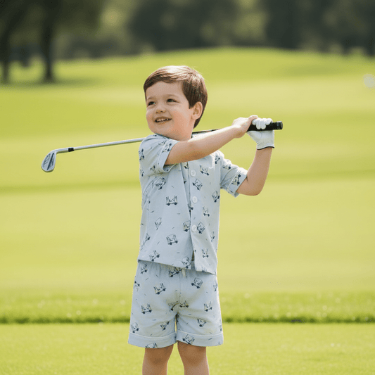 Toddler boy playing golf on a green while wearing the Tatum Boy Golf Short Set, featuring a light blue golf cart print shirt and coordinating shorts, designed for comfortable active play.