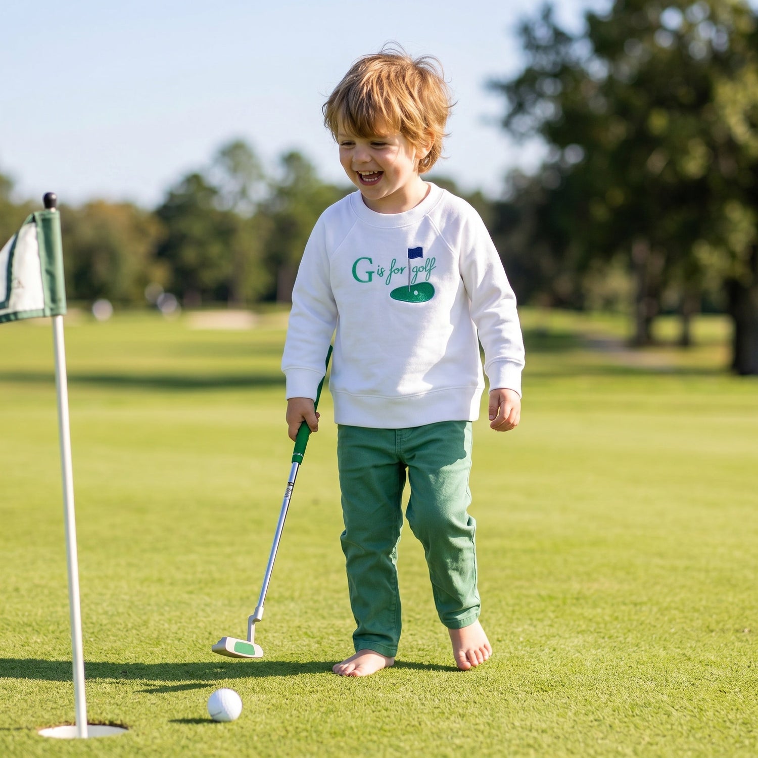 Toddler wearing a golf themed sweatshirt that says G is for Golf. With a green and pin flag. 