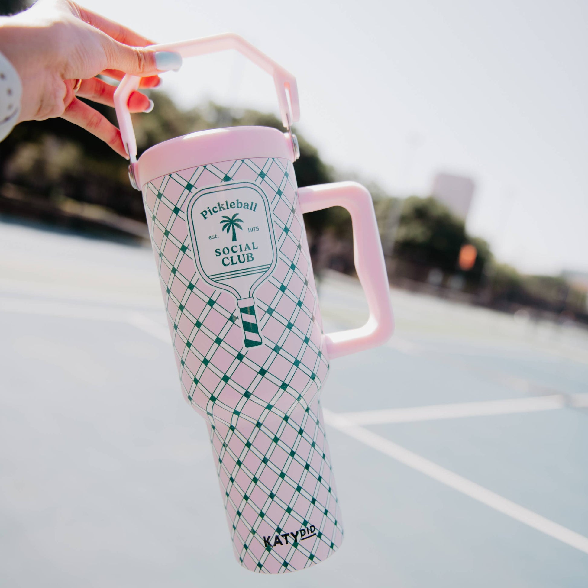 Pink and green 'Pickleball Social Club' mug held by a hand on a tennis court.