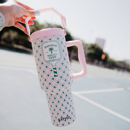 Pink and green 'Pickleball Social Club' mug held by a hand on a tennis court.