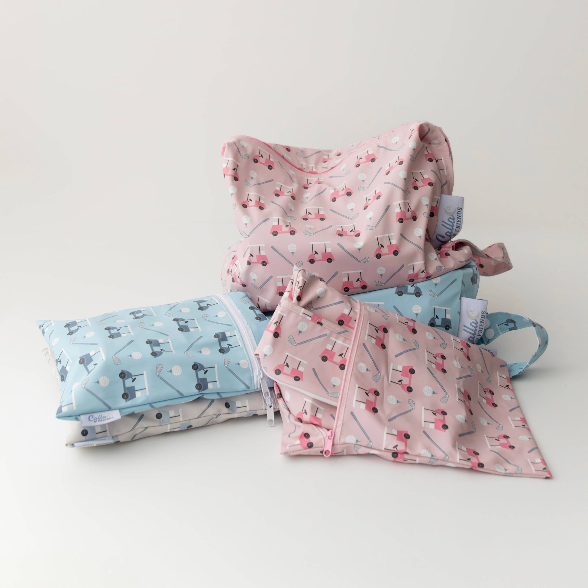 Set of 3 wet/dry bags with golf cart pattern on  white background. Bags are pink, blue, and grey.