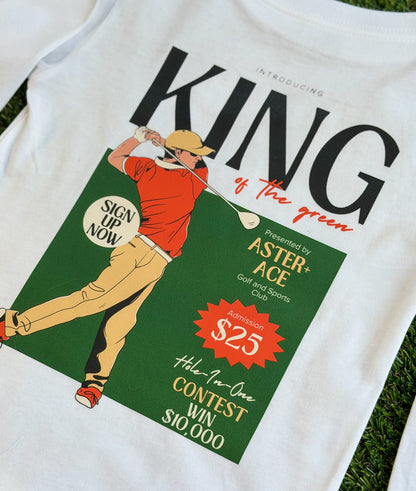 Back of boys’ King of the Green white golf t-shirt featuring a retro-style “King of the Green” graphic with a golfer illustration in red and tan, green background, and vintage tournament-style text.