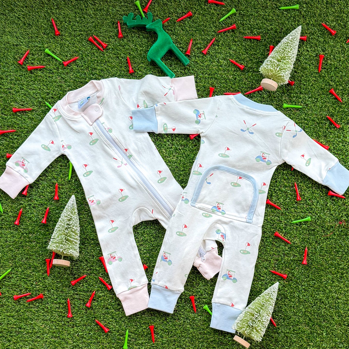 Set of Aster and Ace holiday golf baby onesies in pink and blue trims with Santa golf cart and golf green pattern, photographed flat lay with Christmas décor.