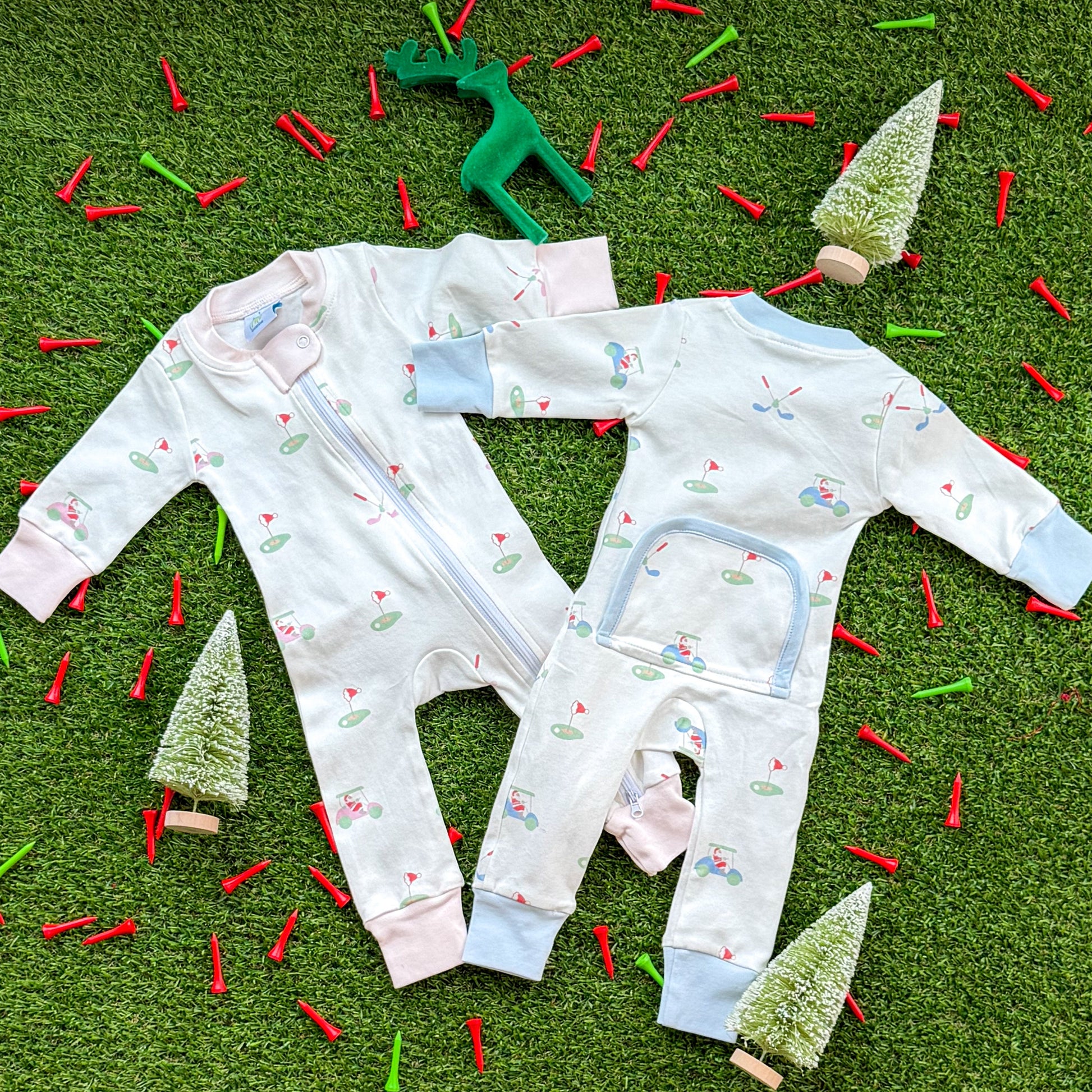 Set of Aster and Ace holiday golf baby onesies in pink and blue trims with Santa golf cart and golf green pattern, photographed flat lay with Christmas décor.