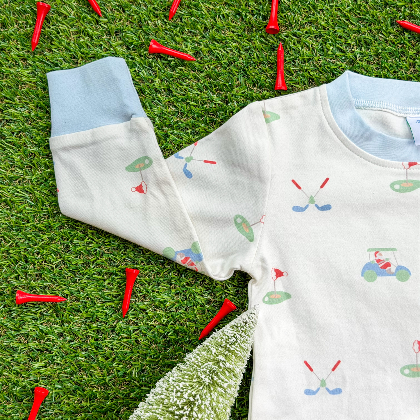 Close-up of a kids’ Christmas golf pajama top made from soft organic cotton, featuring light blue cuffs and playful Santa golfing print with golf clubs, greens, and carts.