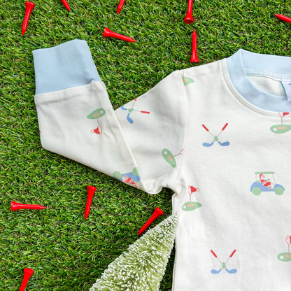Close-up of a kids’ Christmas golf pajama top made from soft organic cotton, featuring light blue cuffs and playful Santa golfing print with golf clubs, greens, and carts.