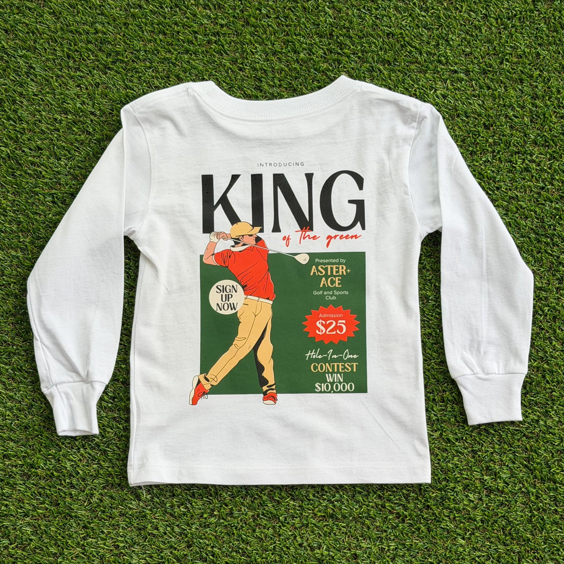 Back of boys’ long sleeve white golf t-shirt featuring a vintage-style “King of the Green” graphic with a golfer in red and tan swinging a club, set against a green background with retro text details.