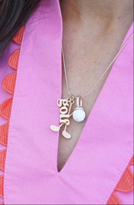 Girl wearing golf themed necklace with 3 charms. One spells out golf, one is a golf ball, and one is crossed clubs. 