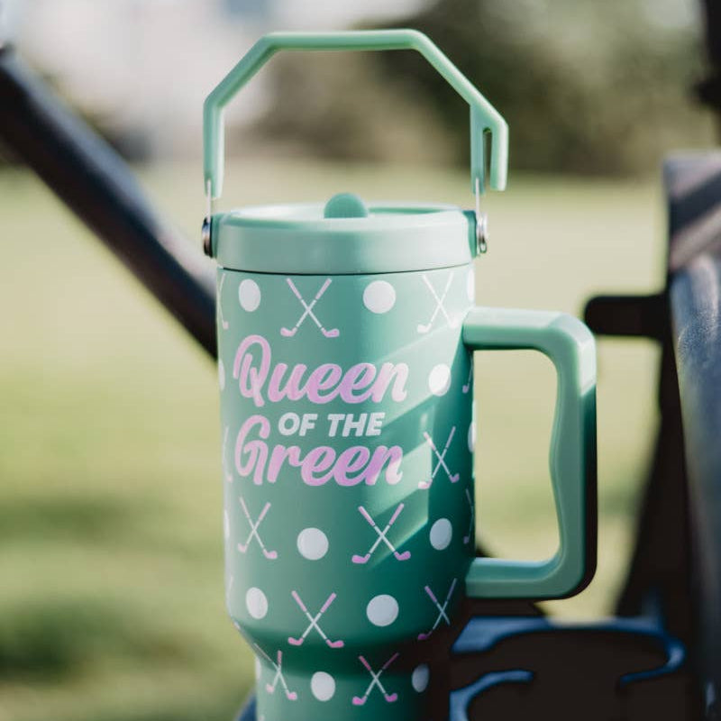 Green “Queen of the Green” golf tumbler with handle sitting on a golf cart, decorated with white dots and crossed golf clubs.