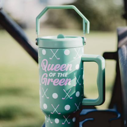 Green “Queen of the Green” golf tumbler with handle sitting on a golf cart, decorated with white dots and crossed golf clubs.
