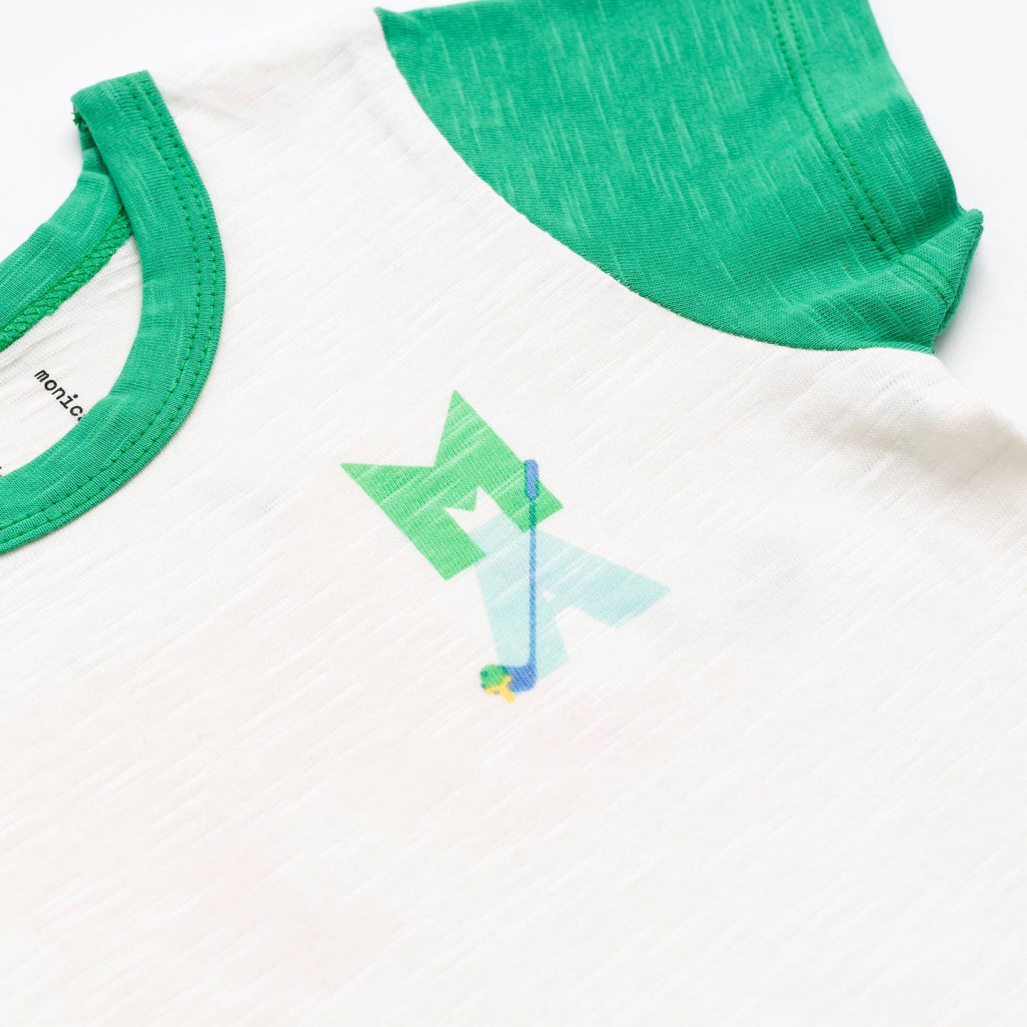 Close-up of Monica and Andy organic cotton kids golf T-shirt with green sleeves and small MA golf club logo on white slub jersey – available at Aster and Ace.