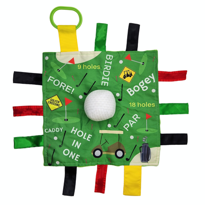 Golf themed sensory lovey for babies. Green background with multi-colored ribbons coming out on the sides. Golf words written on it and a squishy golf ball in the middle. 