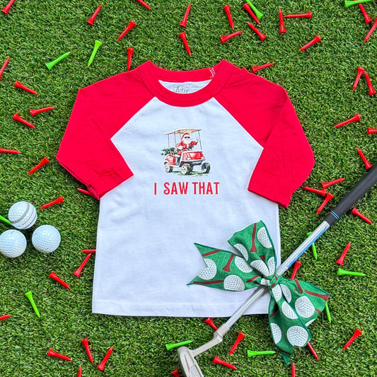Red-and-white kids’ baseball tee featuring a Santa golf cart graphic and the text “I Saw That,” displayed on turf with red and green golf tees, golf balls, and a golf club with a green bow.