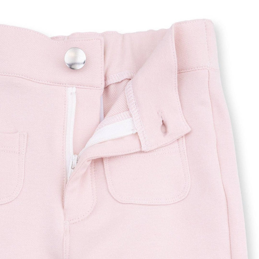 Close up of light pink pants with silver button closure and white zip fly