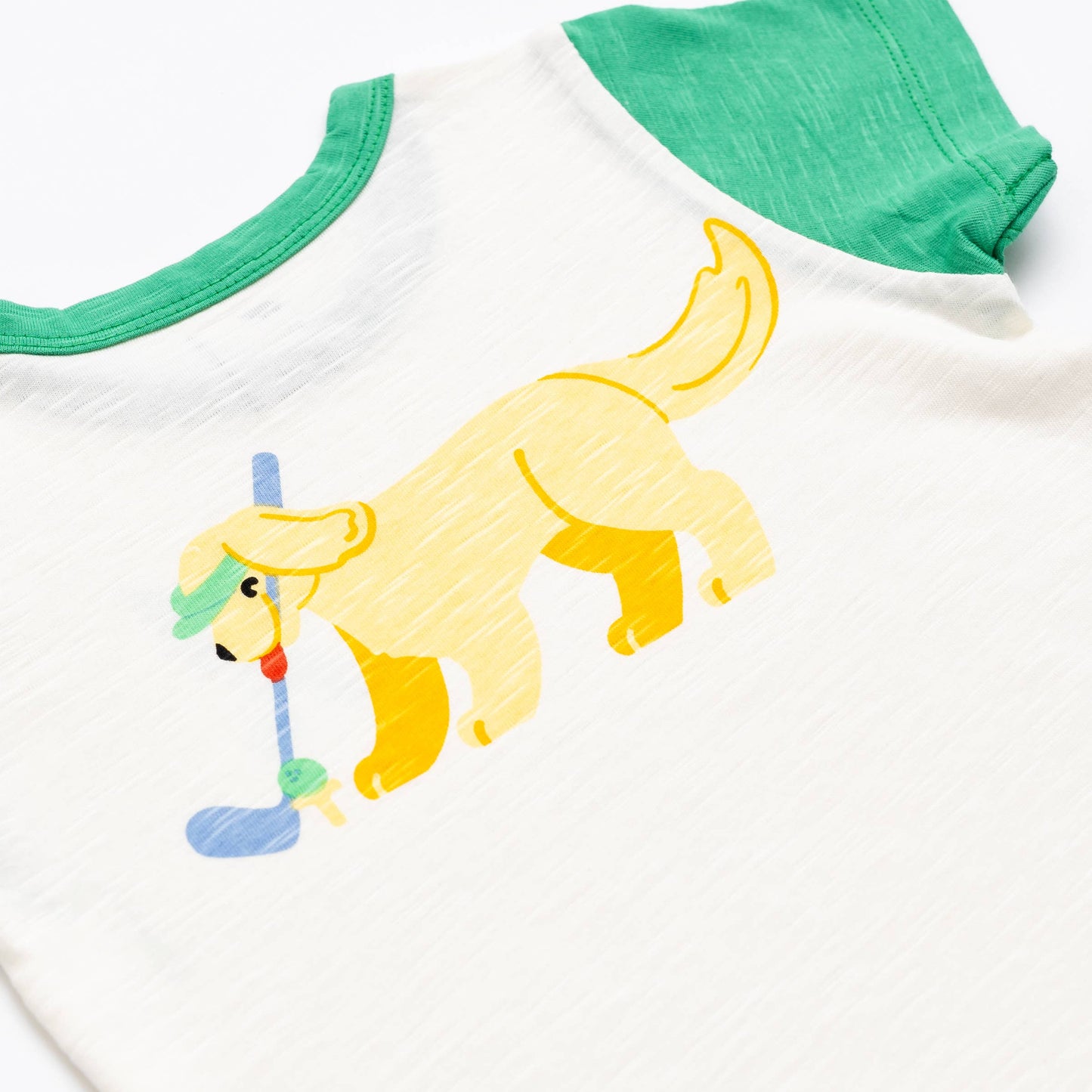 Kids organic cotton golf T-shirt featuring yellow dog playing golf graphic on white slub jersey with green sleeves – Monica and Andy tee at Aster and Ace.