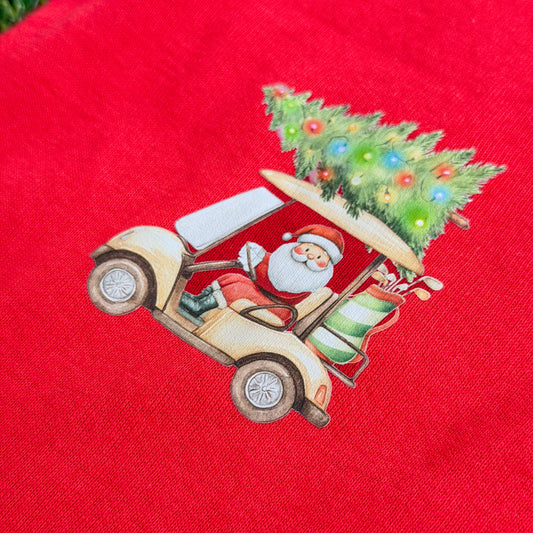 Red baby coverall featuring Santa driving a golf cart with a Christmas tree and holiday lights on top, shown in a close-up on fabric.
