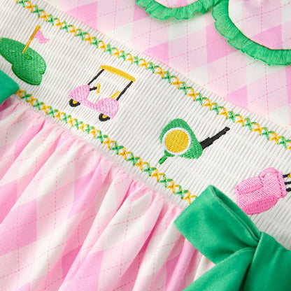 Close-up of pink smocked dress with embroidered golf icons, green trim, and bow detail