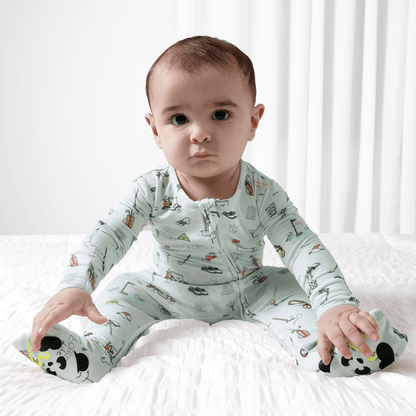 Baby wearing a golf patterned onesie sitting on a white surface with a white curtain in the background.