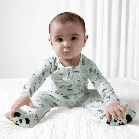 Baby wearing a golf patterned onesie sitting on a white surface with a white curtain in the background.