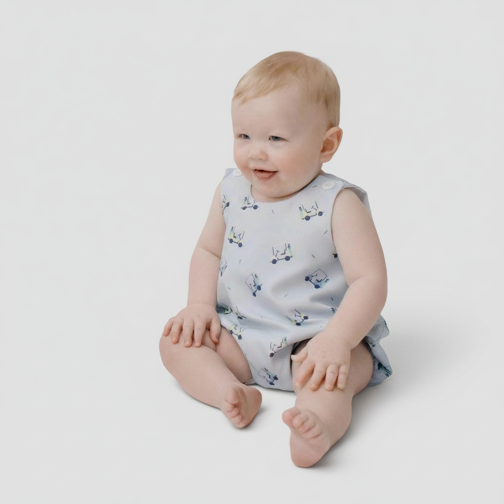 Smiling baby wearing blue golf cart print playsuit from the Tatum Collection, soft cotton outfit for special moments