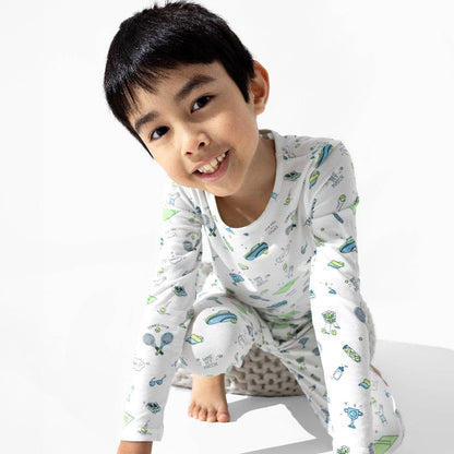 Boy wearing white pajamas with green and blue cartoon tennis pattern on white background