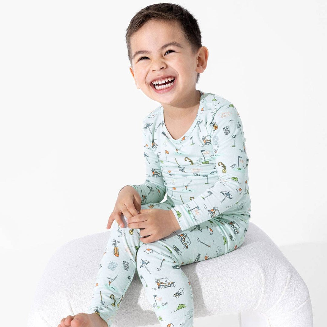 Boy wearing 2 piece light blue pajama set with golf themed cartoon doodles