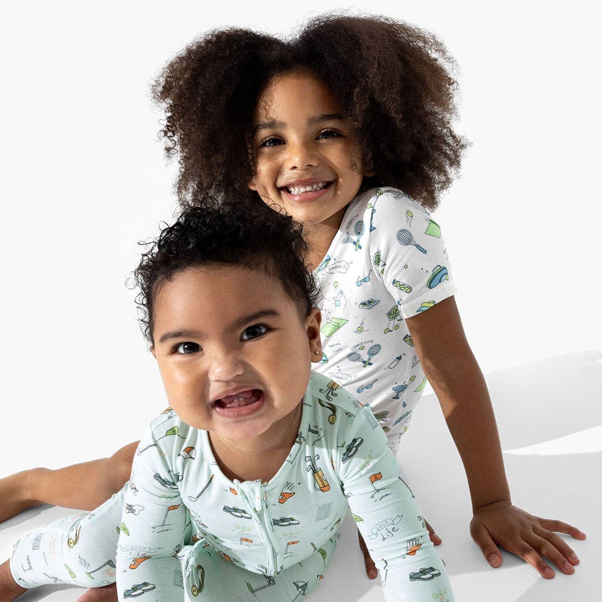 Two children wearing golf and tennis patterned pajamas on a white background
