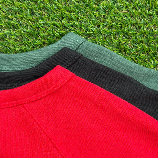 Close-up of three shirt collars in holiday colors—red, black, and heather forest green—displayed on green turf.