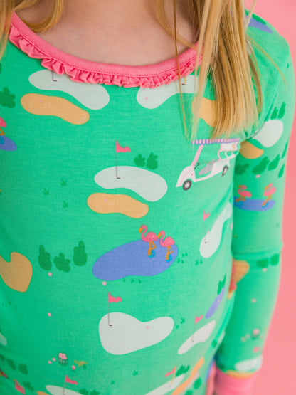 Close up shot of top of golf course pattern sleepwear. Green with blue water with flamingos, golf carts, bunkers, and greens with pink pin flags. Pink ruffle trim around the neck. 