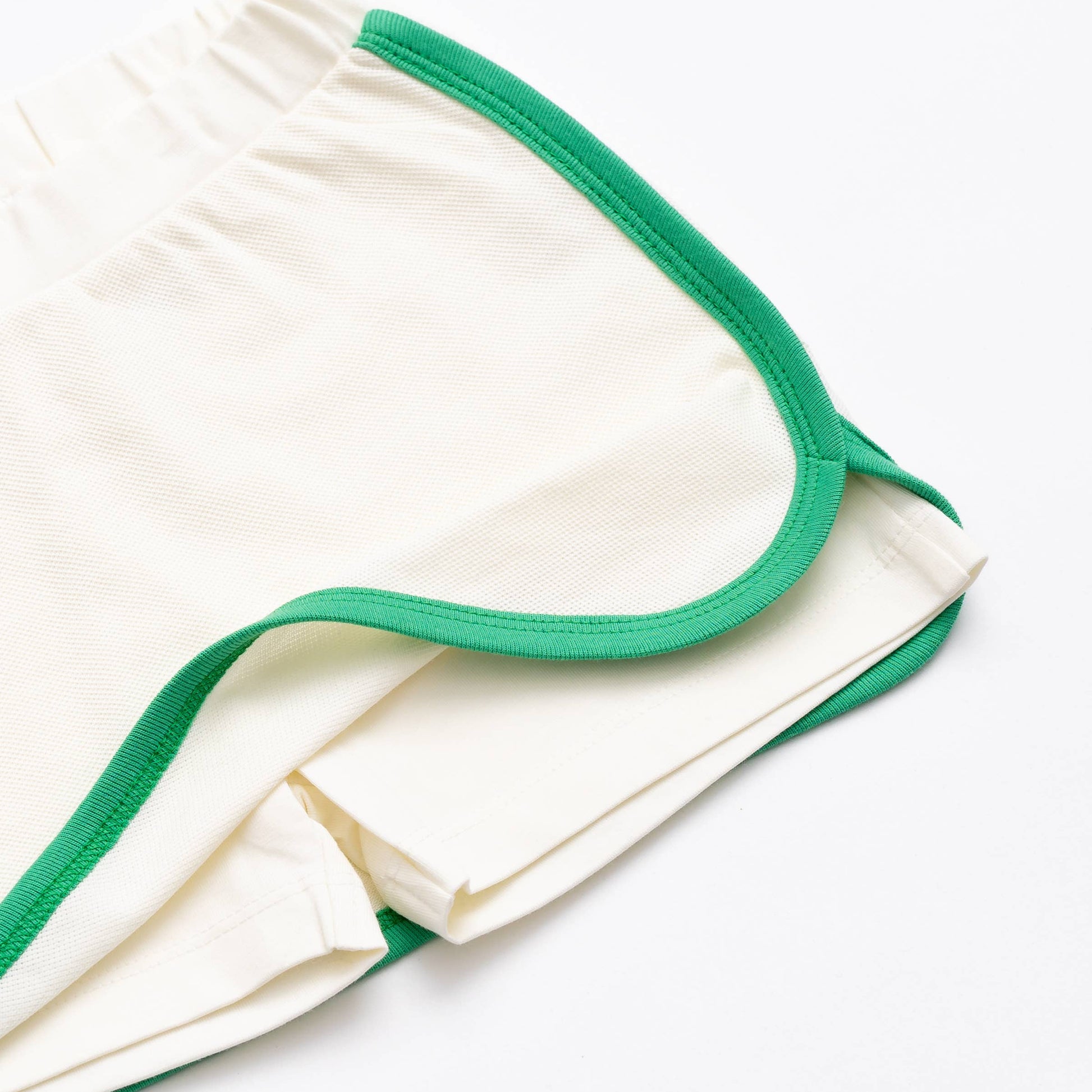 Close-up of Monica + Andy organic cotton girls’ sport skort in ivory with green trim showing breathable pique fabric and built-in shorts.