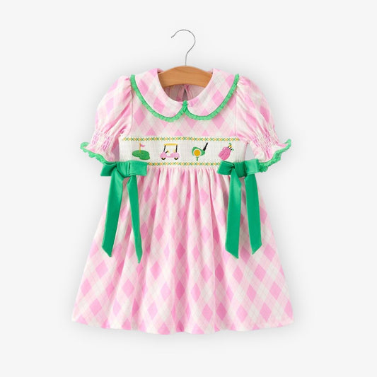 Front view of pink smocked girls dress with embroidered golf details and green bow accents