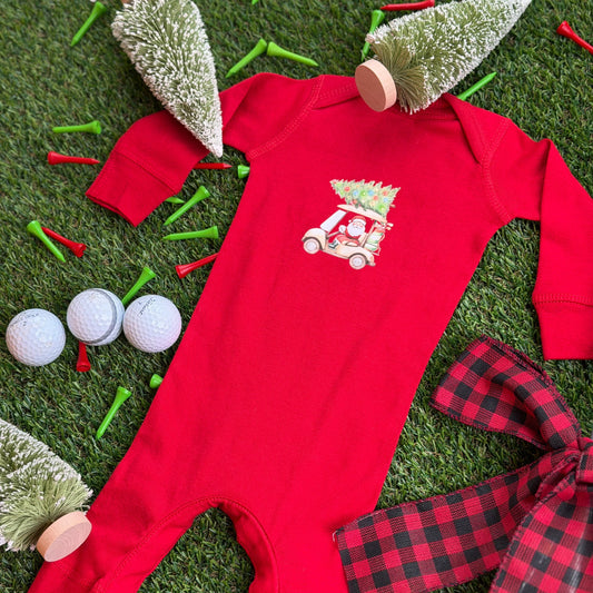 Red baby Christmas golf cart coverall with Santa driving and a decorated tree on top, displayed on turf with holiday décor, golf balls, tees, and small bottlebrush trees.