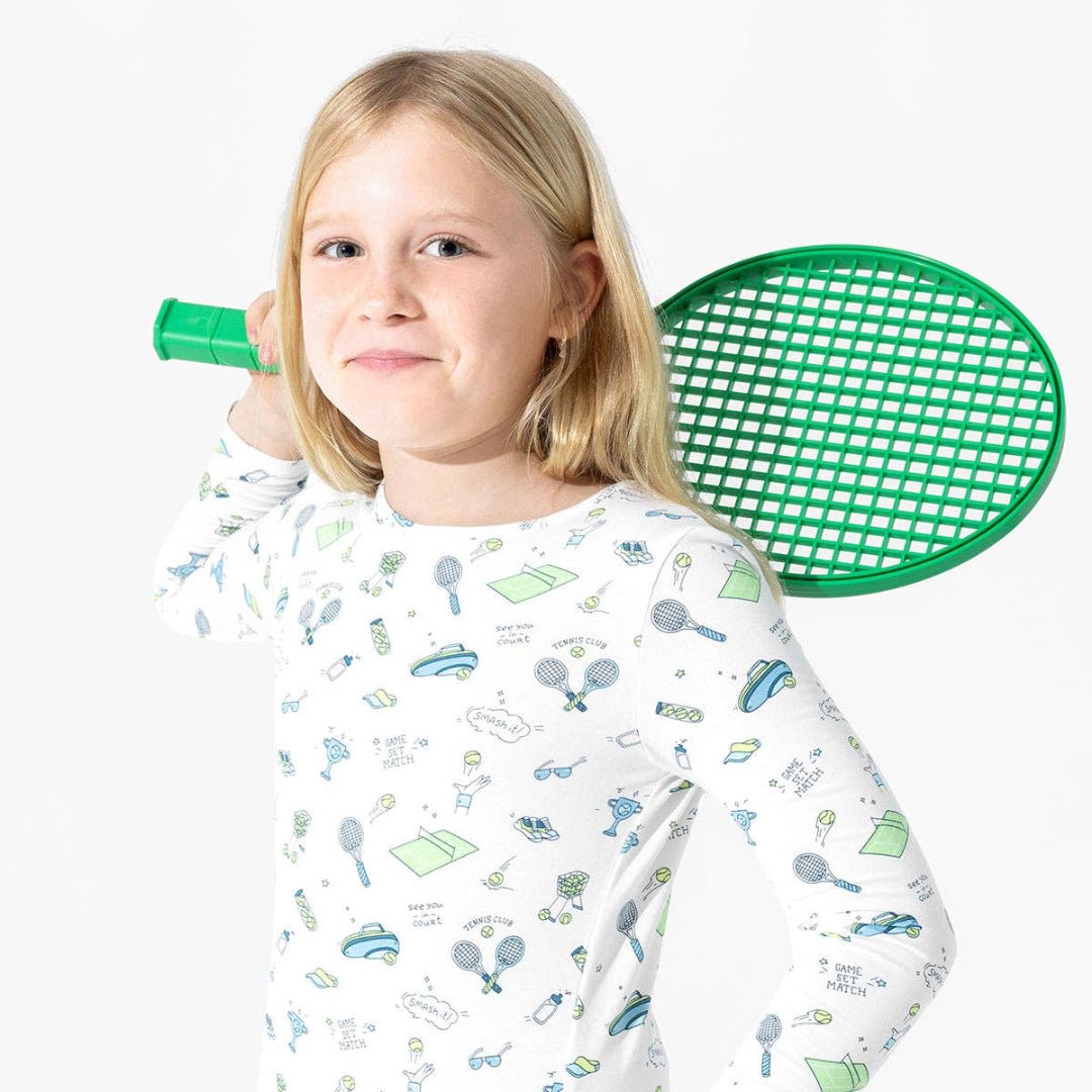Girl wearing white pajamas with blue and green cartoon tennis pattern. 