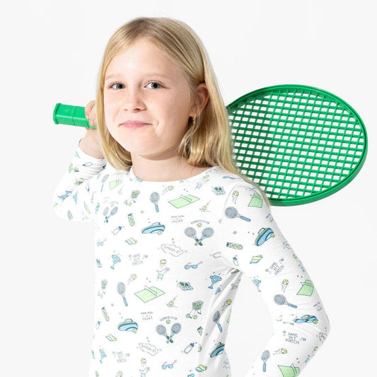 Girl wearing white pajamas with blue and green cartoon tennis pattern. 