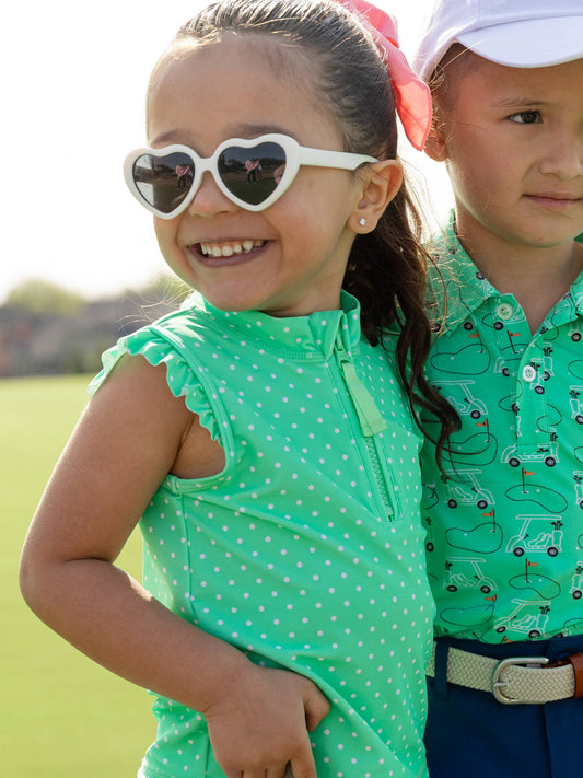 Kids in golf outfits. Girl wearing green athletic shirt with white polka dots and ruffle sleeves on a golf course