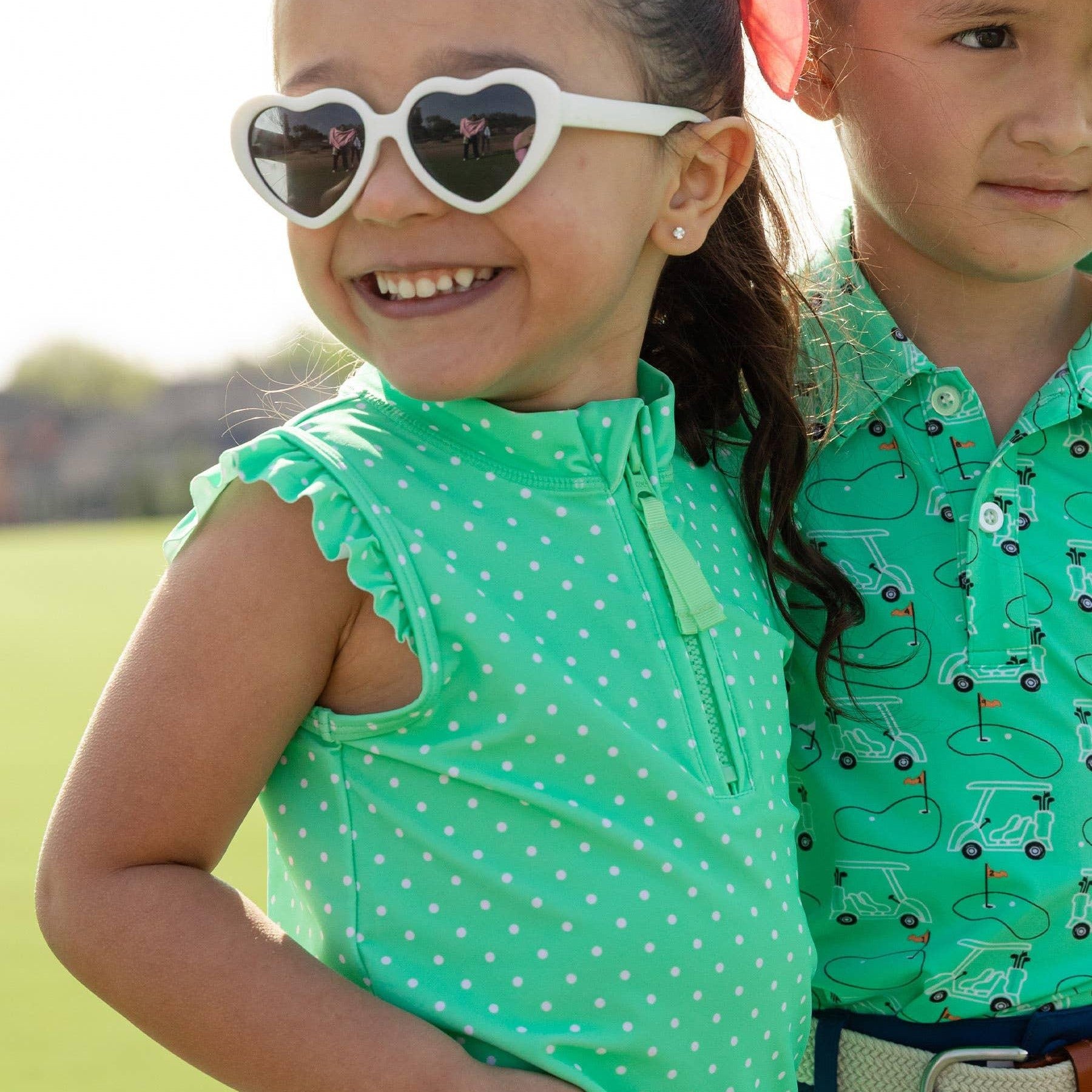 Kids in golf outfits. Girl wearing green athletic shirt with white polka dots and ruffle sleeves on a golf course 