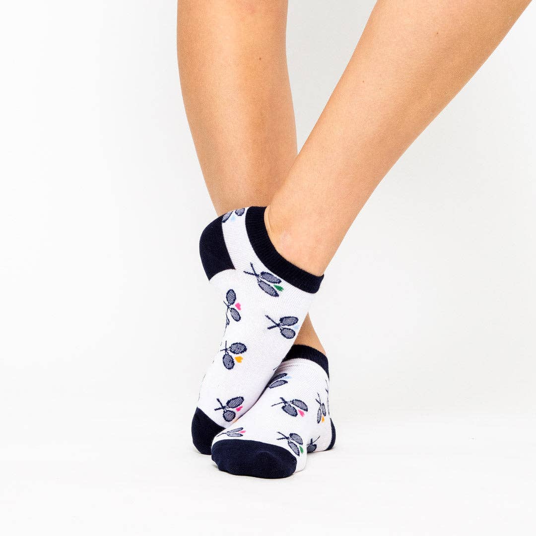 Person wearing white ankle socks with navy trim and tennis racket pattern, shown standing with crossed ankles