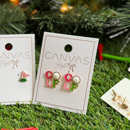 Golf-themed stud earrings from Canvas Style displayed on product cards, including colorful “GOLF” letter earrings with golf ball details and a pink 18th hole flag earring, photographed on artificial grass with a Christmas tree background for a festive gift look.