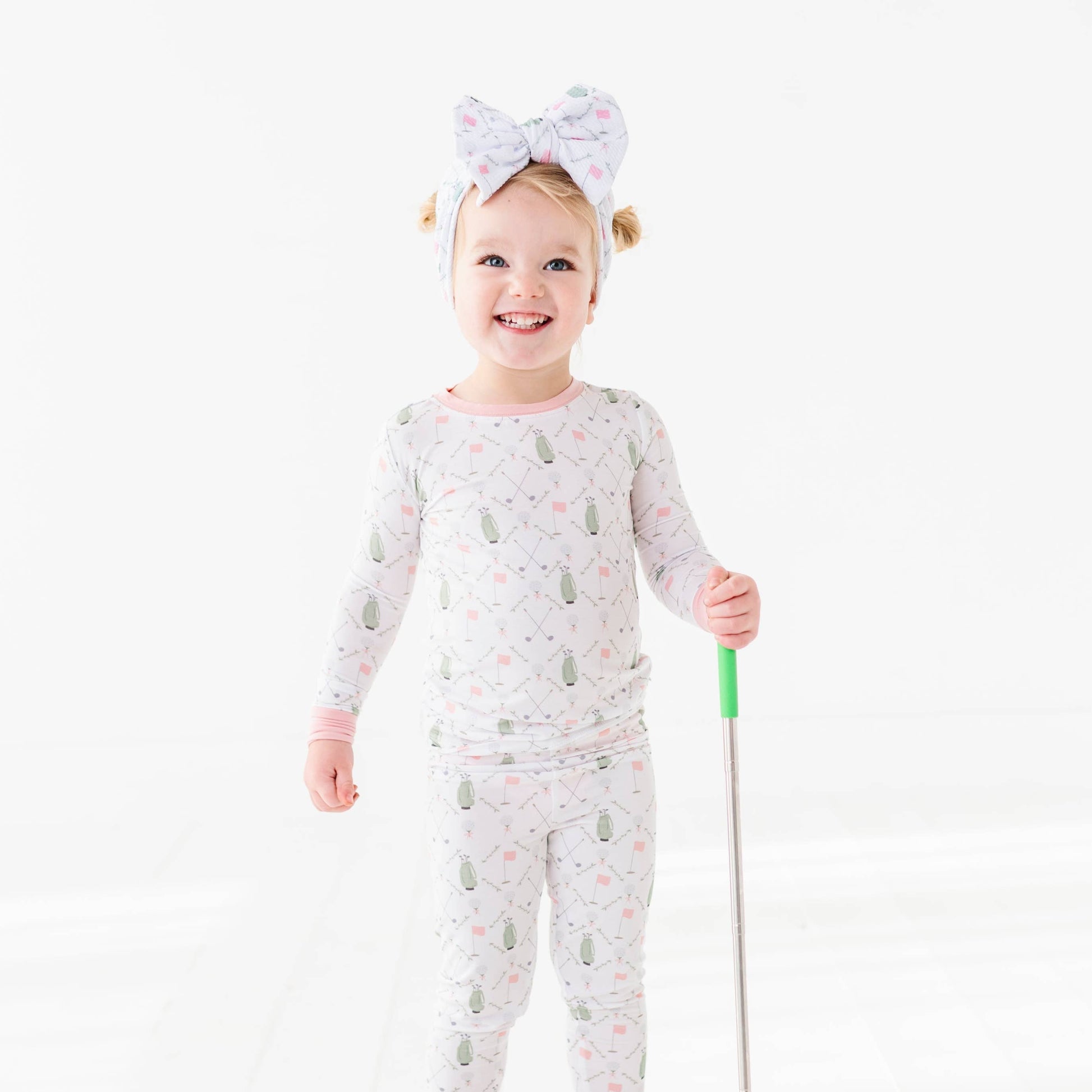 girl wearing girls pink and white golf pajamas with green golf bags