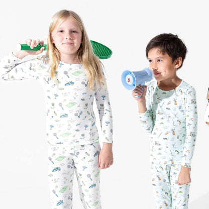 2 kids wearing pajamas. One has white pajamas with tennis icon doodles and the other has light blue pajamas with golf icon doodles.