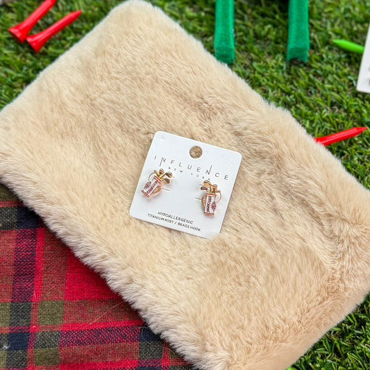 Golf-themed stocking stuffer flat lay featuring Influence New York pink golf bag stud earrings displayed on a fuzzy cream pouch with red plaid trim, surrounded by green turf and red golf tees.