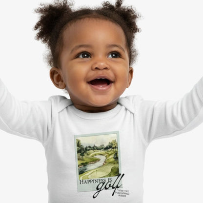 Baby wearing white Aster and Ace “Happiness Is Golf” coverall with illustrated golf course graphic, smiling with arms raised.