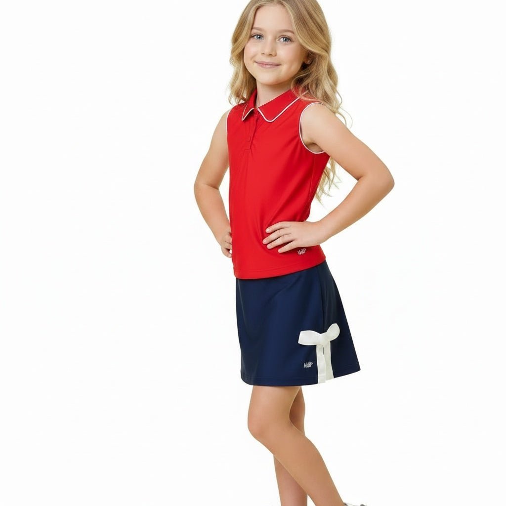 Girl wearing navy athletic skirt with white bow detail and red top on white background
